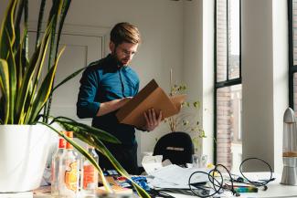 a man standing in an office holding a box by Tim van der Kuip courtesy of Unsplash.