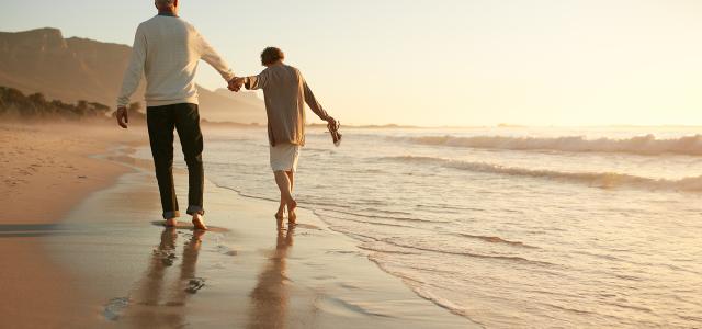 Retired couple walking on beach at sunset